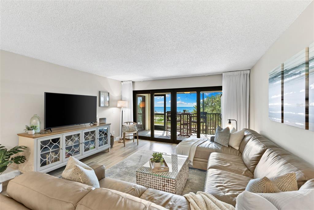 A living room features a sectional sofa, a media console, and a balcony with ocean views — 900 GULF BLVD UNIT 104, INDIAN ROCKS BEACH, FL