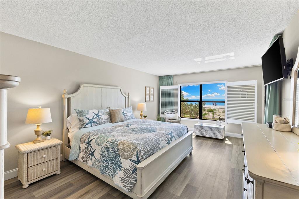 A bedroom with a king bed, coastal bedding, wicker nightstand, and a view of the beach — 900 GULF BLVD UNIT 104, INDIAN ROCKS BEACH, FL