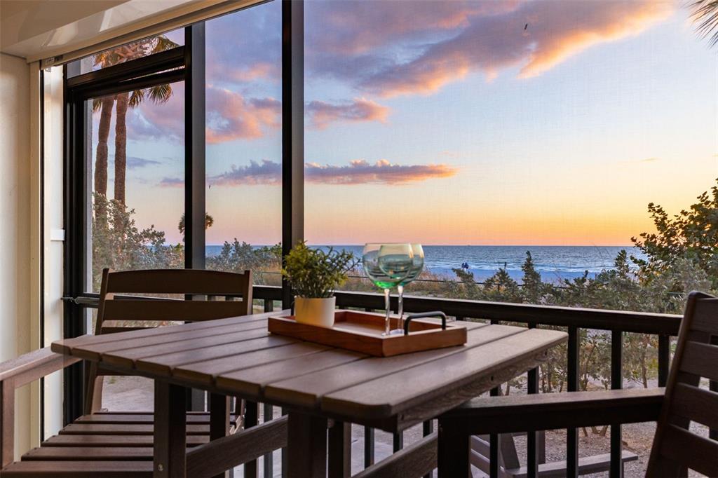 A wooden table with two glasses and a plant sits on a screened-in balcony overlooking the ocean — 900 GULF BLVD UNIT 104, INDIAN ROCKS BEACH, FL