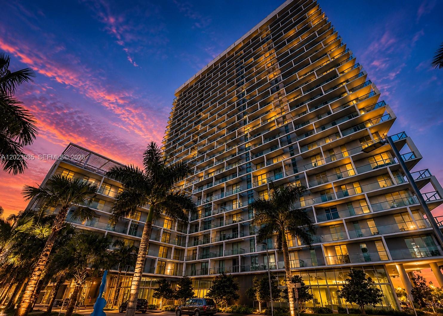 A low-angle view of a modern high-rise apartment building at sunset with palm trees — 2000 Metropica Way # 1408, Sunrise FL 33323, SUNRISE, FL