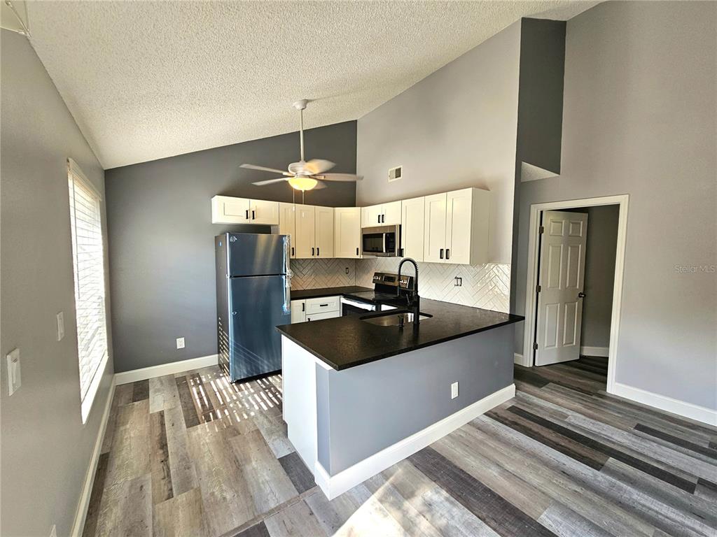 A kitchen features white cabinets, black countertops, stainless steel appliances, and wood-look flooring — 2668 MEGAN COURT, PALM HARBOR, FL