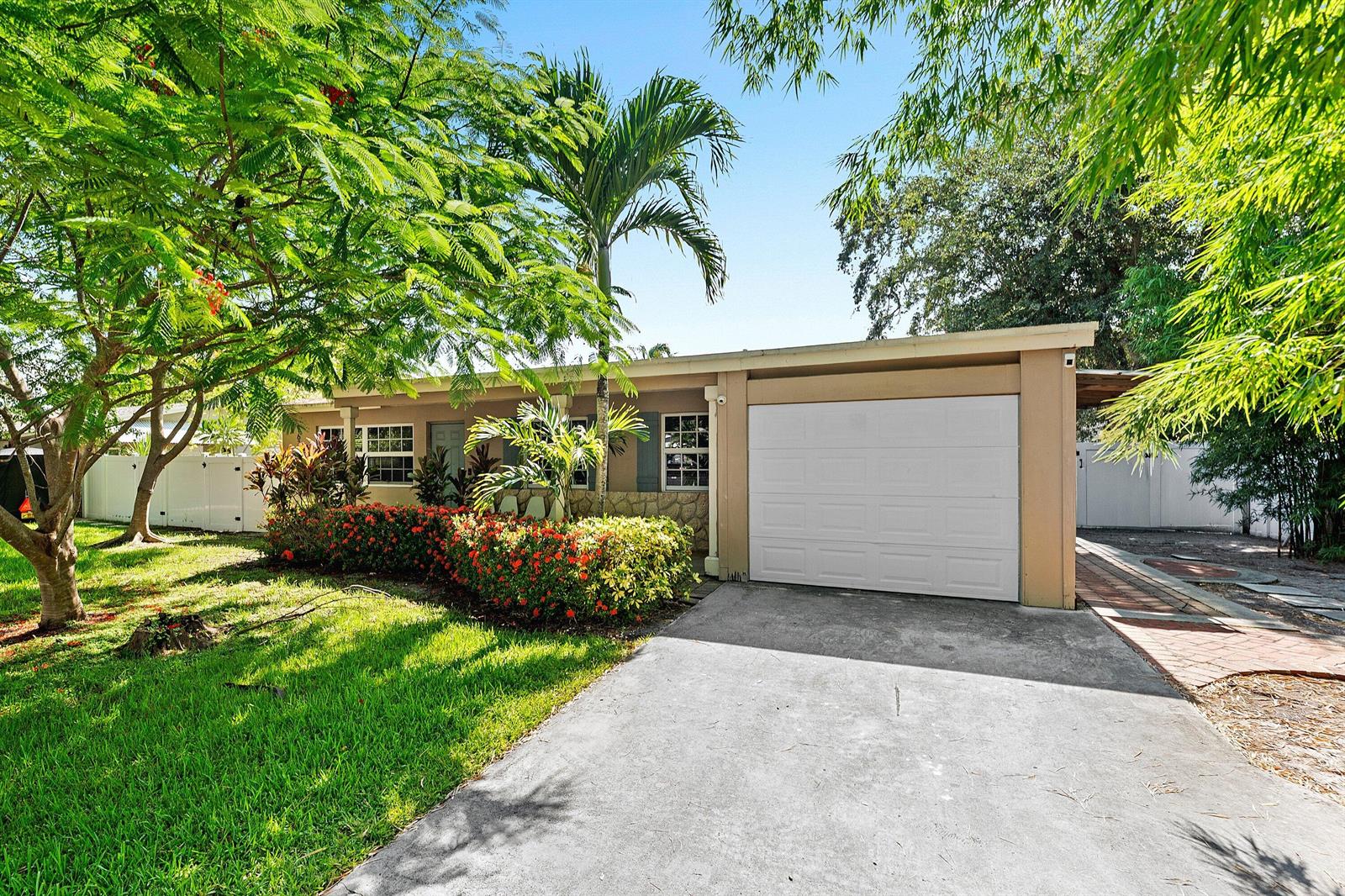 A single-story house with a white garage door, a concrete driveway, and lush tropical landscaping — 1638 NE 3rd Avenue, Delray Beach FL 33444, DELRAY BEACH, FL