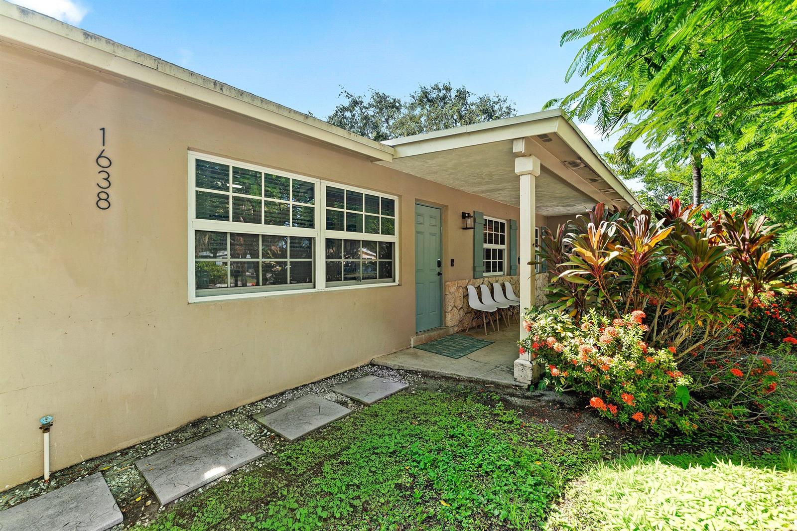 A tan house exterior features a covered porch, a light blue door, and landscaping — 1638 NE 3rd Avenue, Delray Beach FL 33444, DELRAY BEACH, FL