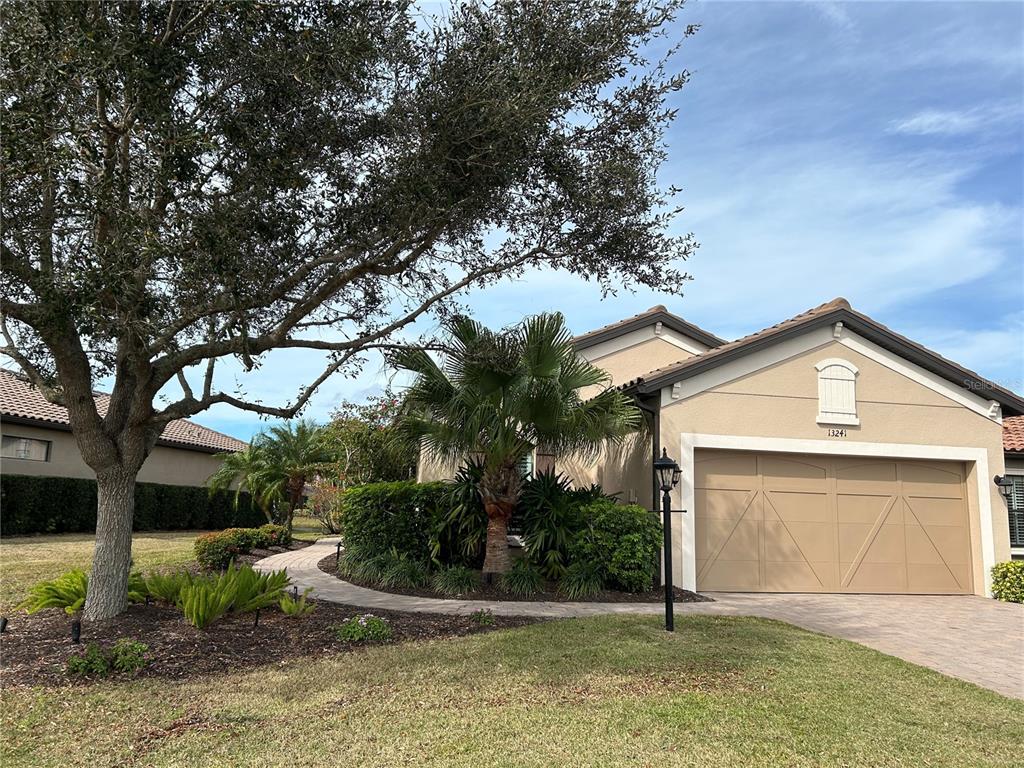 A paved walkway leads along the side of a house with landscaping and flowering bushes — 13241 TORRESINA TERRACE, BRADENTON, FL