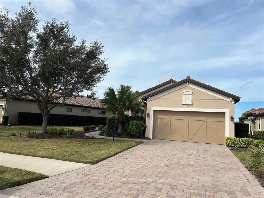 A beige single-story house features a front entrance with a paved walkway and landscaping — 13241 TORRESINA TERRACE, BRADENTON, FL