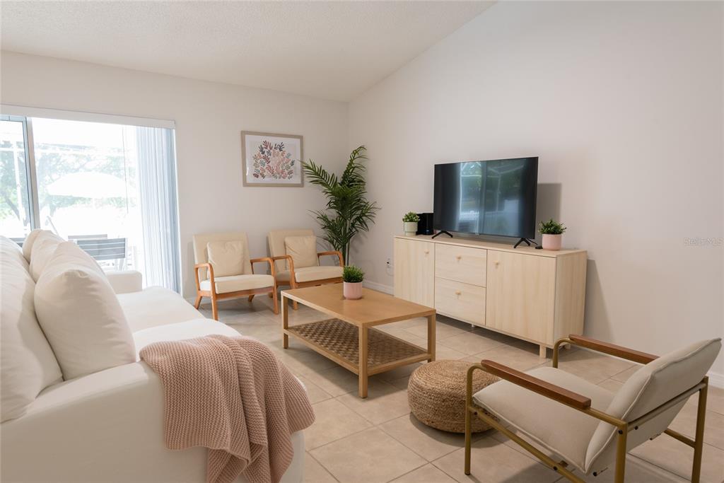 A bright living room features a white sofa, two armchairs, a coffee table, and television — 1085 INDIAN RIDGE TRL E, KISSIMMEE, FL