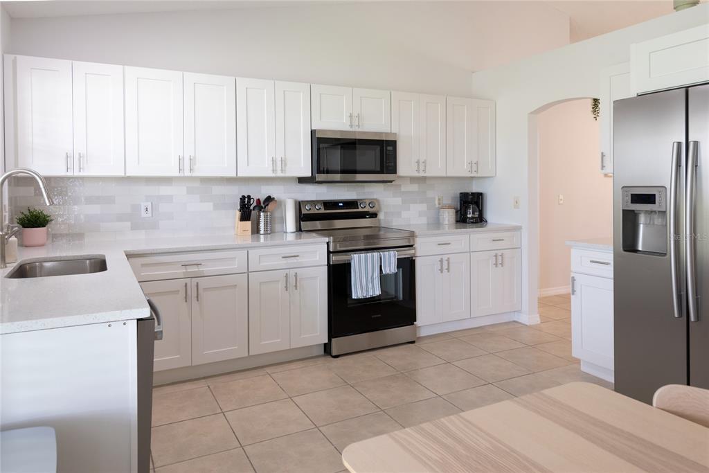 A kitchen features white cabinets, stainless steel appliances, a tiled backsplash, and light-colored countertops — 1085 INDIAN RIDGE TRL E, KISSIMMEE, FL