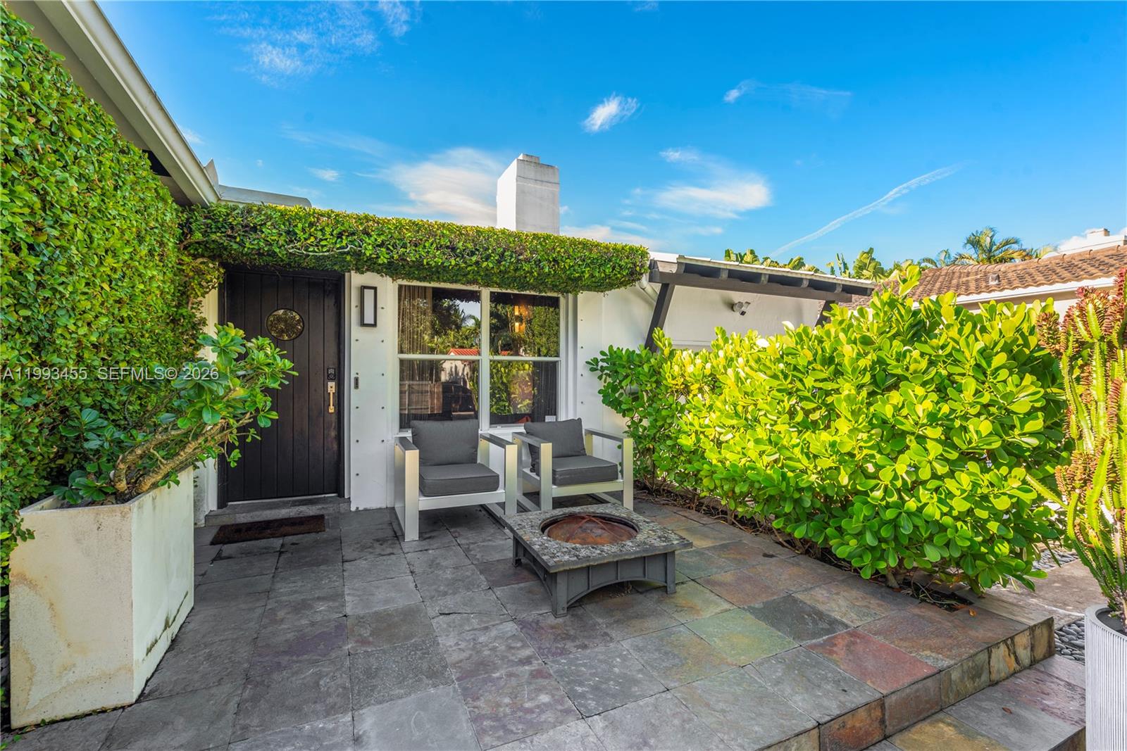 A patio features two chairs, a fire pit, and lush greenery in front of a house — 738 NE 72nd Ter, Miami FL 33138, MIAMI, FL