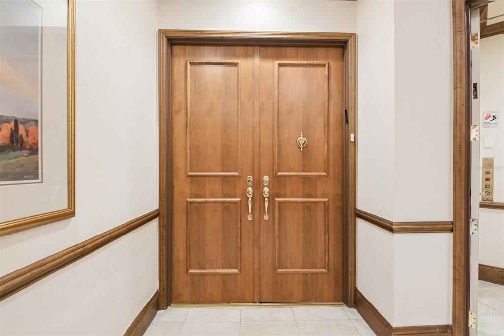 A set of wooden double doors with brass hardware is centered in a tiled hallway — 1180 GULF BOULEVARD UNIT 101, CLEARWATER BEACH, FL