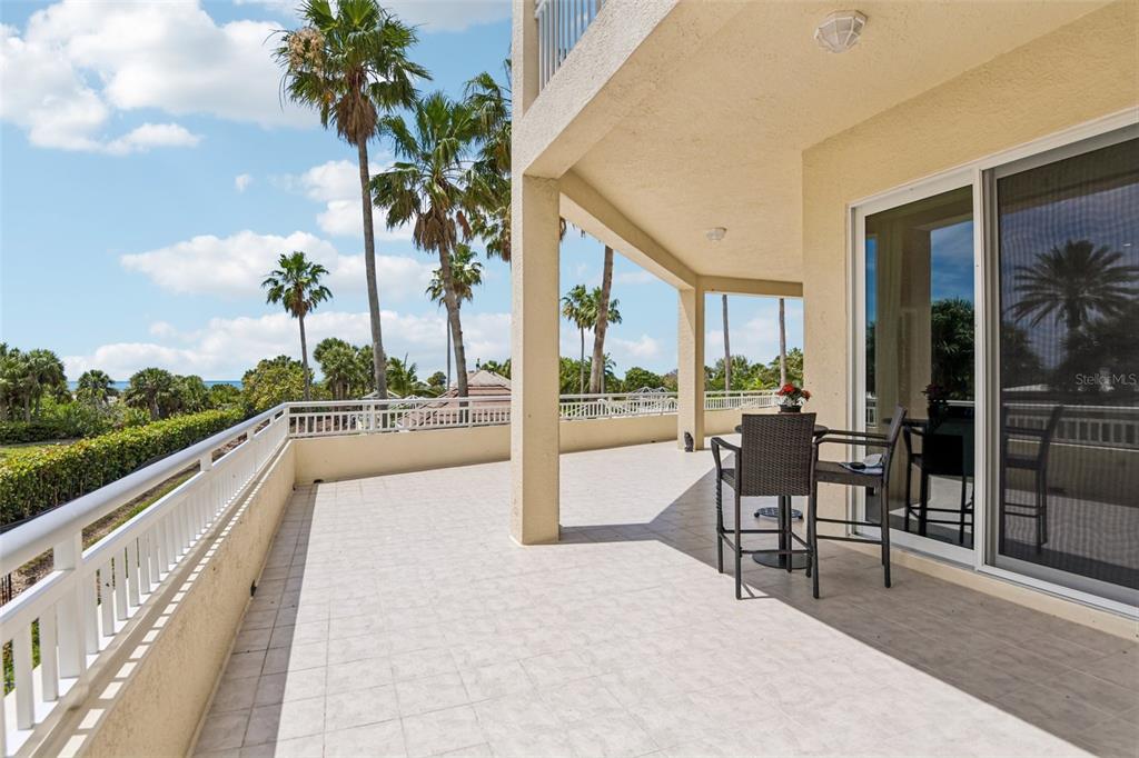 A spacious, tiled balcony features a small bistro set and views of palm trees — 1180 GULF BOULEVARD UNIT 101, CLEARWATER BEACH, FL