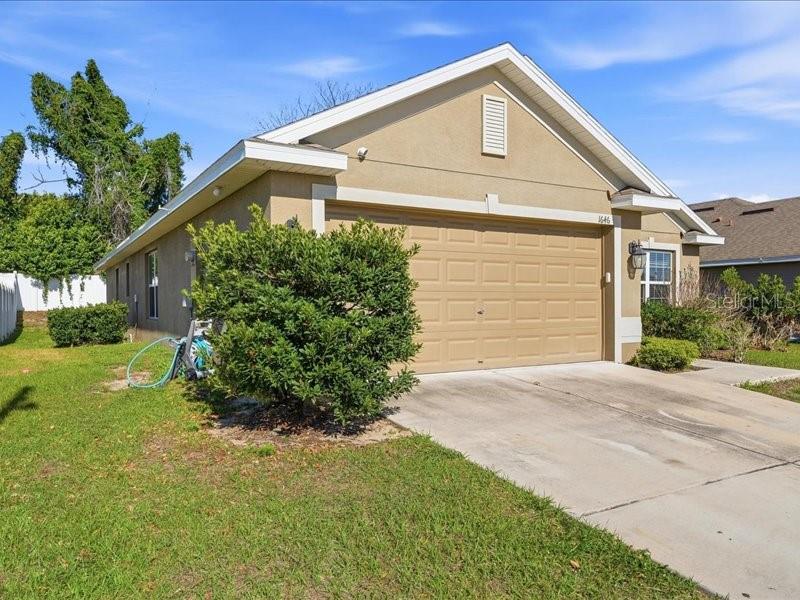A tan, single-story house features a two-car garage and a large green bush in front — 1646 TRESSEL COURT, WINTER HAVEN, FL