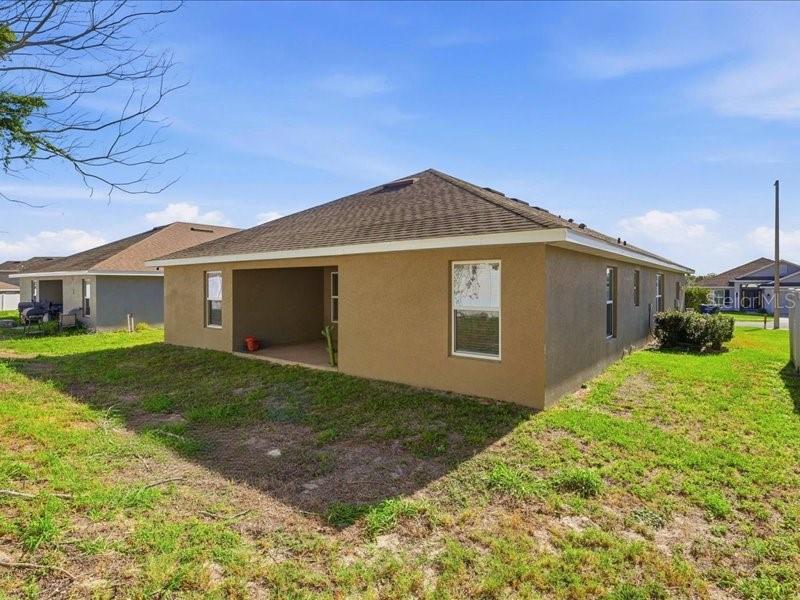 The rear exterior of a tan stucco house features a covered patio and a yard — 1646 TRESSEL COURT, WINTER HAVEN, FL