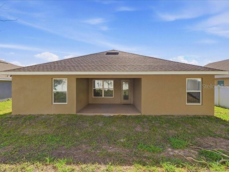 The rear exterior of a single-story house features a covered patio, stucco walls, and windows — 1646 TRESSEL COURT, WINTER HAVEN, FL