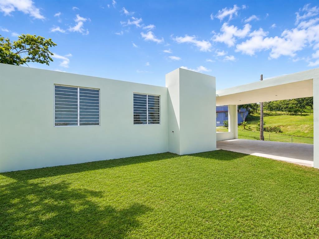 A light green exterior wall with two windows sits beside a covered concrete carport — 115 km 13.2 BO PUEBLO, RINCON, PR