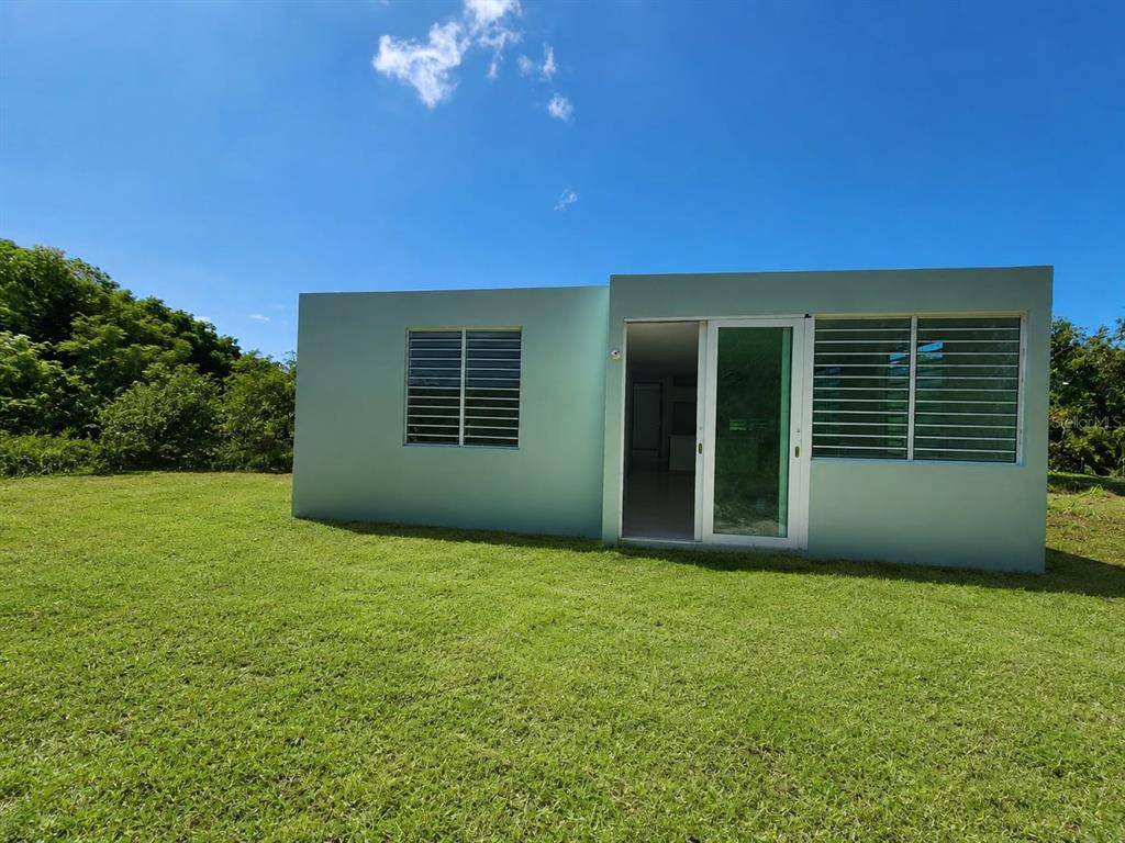 A light green, flat-roofed house stands in a grassy yard under a blue sky — 115 km 13.2 BO PUEBLO, RINCON, PR