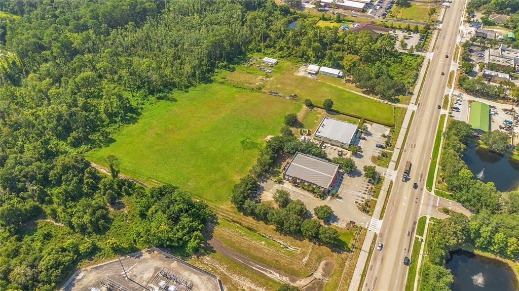 An aerial view shows a large, grassy vacant lot adjacent to commercial buildings and woods — ROCK SPRINGS ROAD, APOPKA, FL