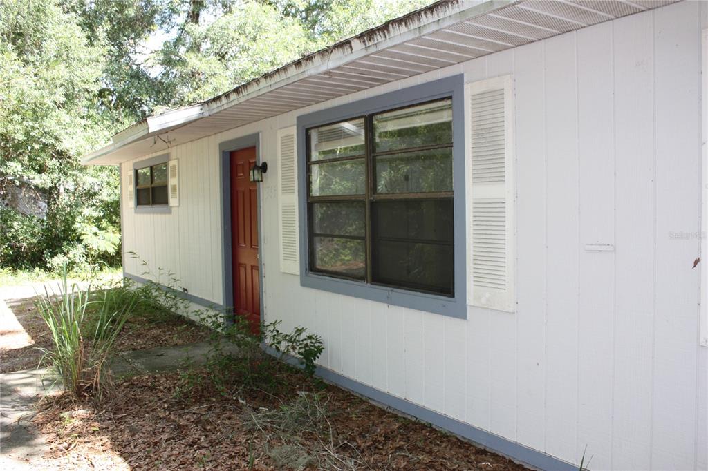 The exterior of a white house features a red front door and a large window — 7965 W FERN PLACE, HOMOSASSA, FL