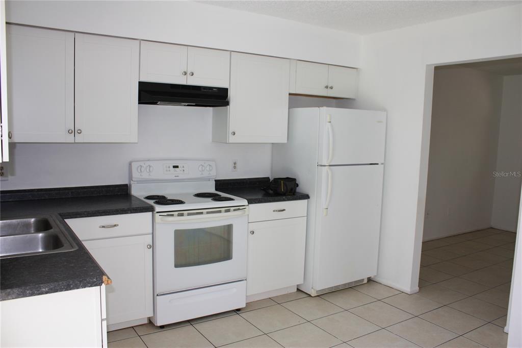 A kitchen features white cabinets, white appliances, and dark countertops over a tiled floor — 7965 W FERN PLACE, HOMOSASSA, FL