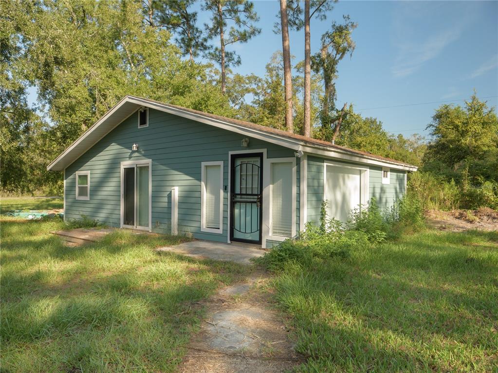 A single-story house with teal siding, a front door with a screen, and overgrown grass — 13117 N COUNTY ROAD 225, GAINESVILLE, FL