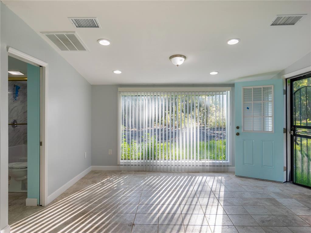 A room with light-colored walls, tiled flooring, a large window with blinds, and a blue door — 13117 N COUNTY ROAD 225, GAINESVILLE, FL