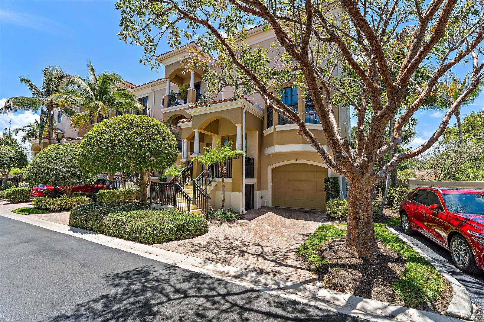 A tan three-story townhouse with a paved driveway, garage, and front stairs under a tree — 605 Del Sol Circle, Tequesta FL 33469, TEQUESTA, FL