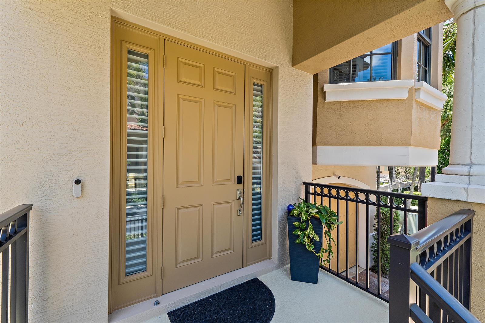 A tan front door with side windows and a potted plant sits on a balcony — 605 Del Sol Circle, Tequesta FL 33469, TEQUESTA, FL