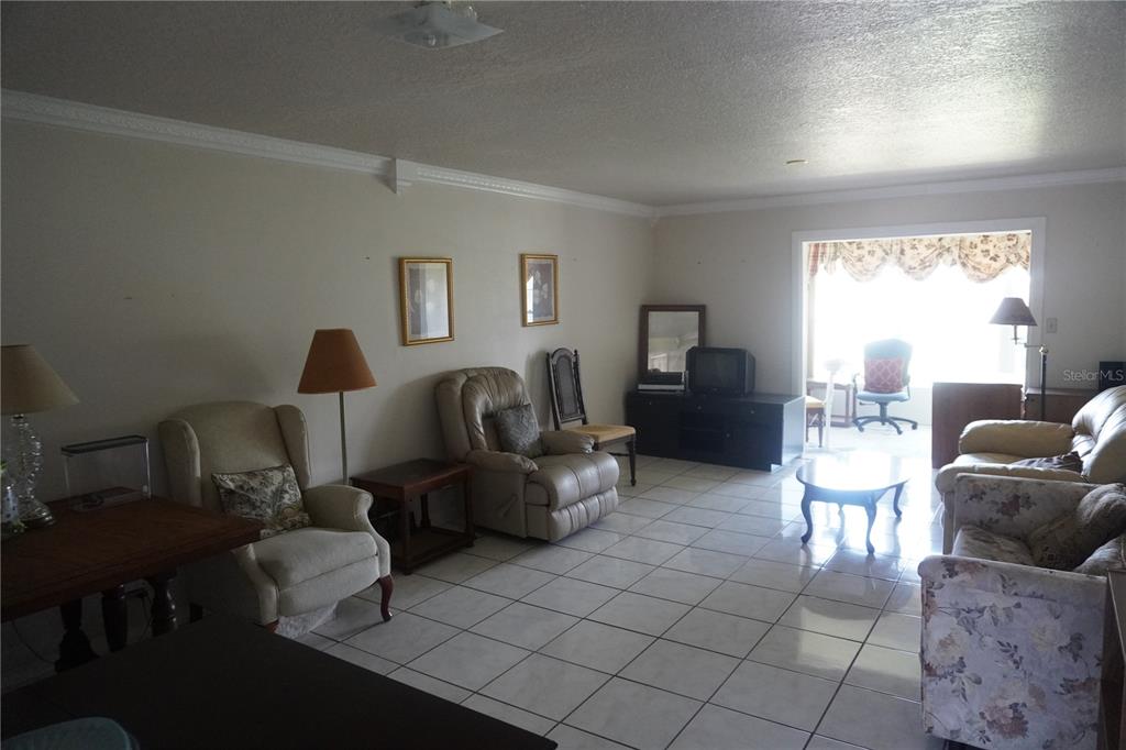 A living room features white tile flooring, beige walls, and several pieces of traditional furniture — 333 LAKE HOWARD DRIVE NW UNIT 303A, WINTER HAVEN, FL