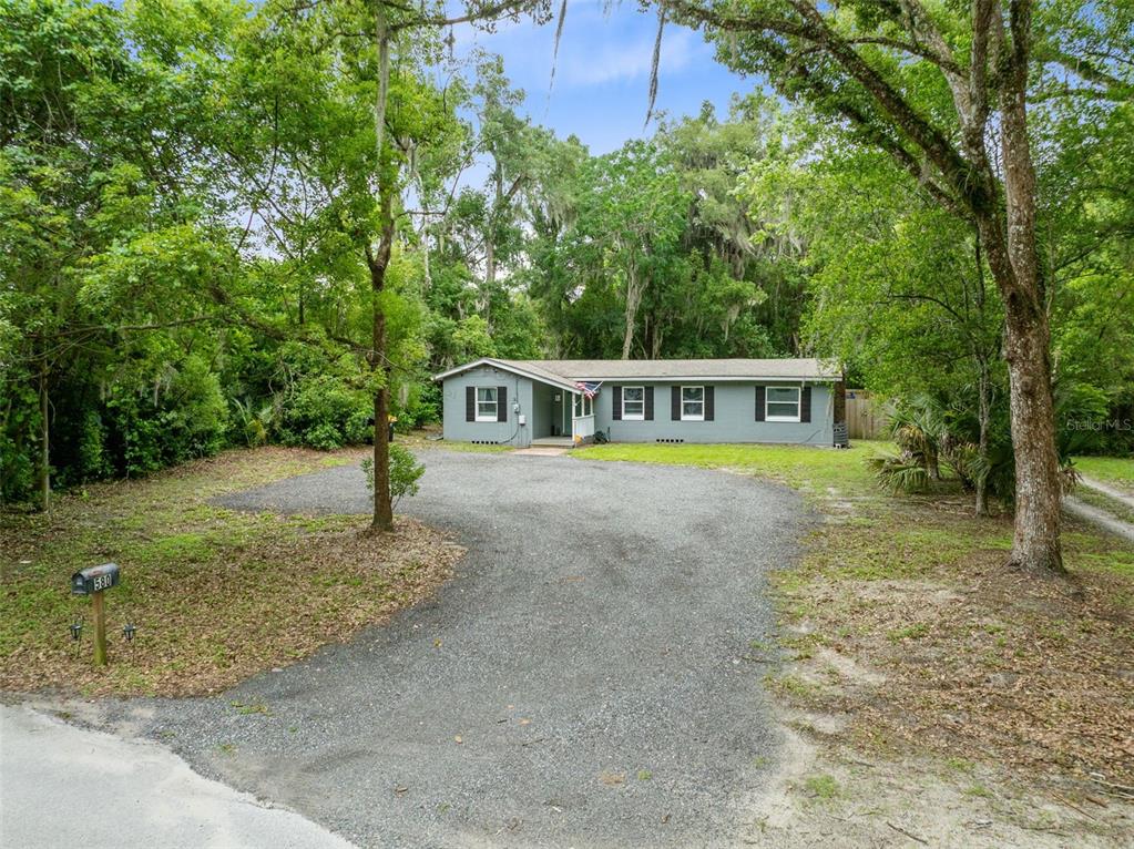 A gray single-story house sits at the end of a long gravel driveway among trees — 580 LAKEVIEW AVENUE, ORANGE CITY, FL