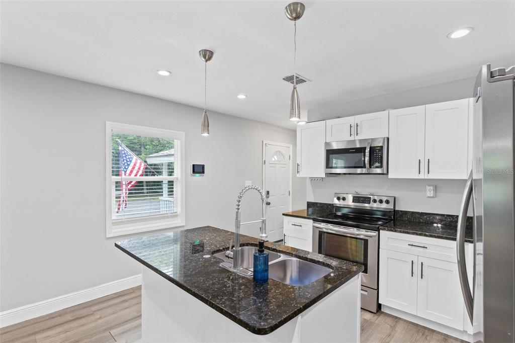 A kitchen features white cabinets, dark granite countertops, a central island, and stainless steel appliances — 580 LAKEVIEW AVENUE, ORANGE CITY, FL