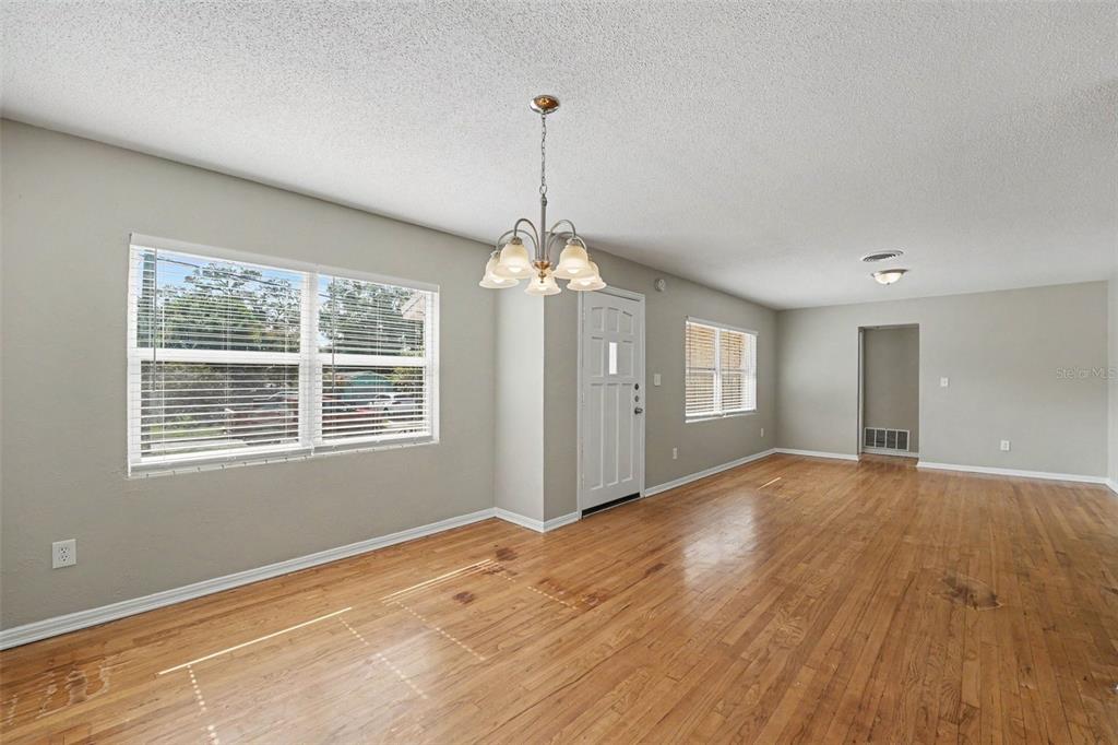 An empty room with hardwood floors, a chandelier, a white front door, and two windows — 2935 WOODLAND HILLS AVENUE, LAKELAND, FL