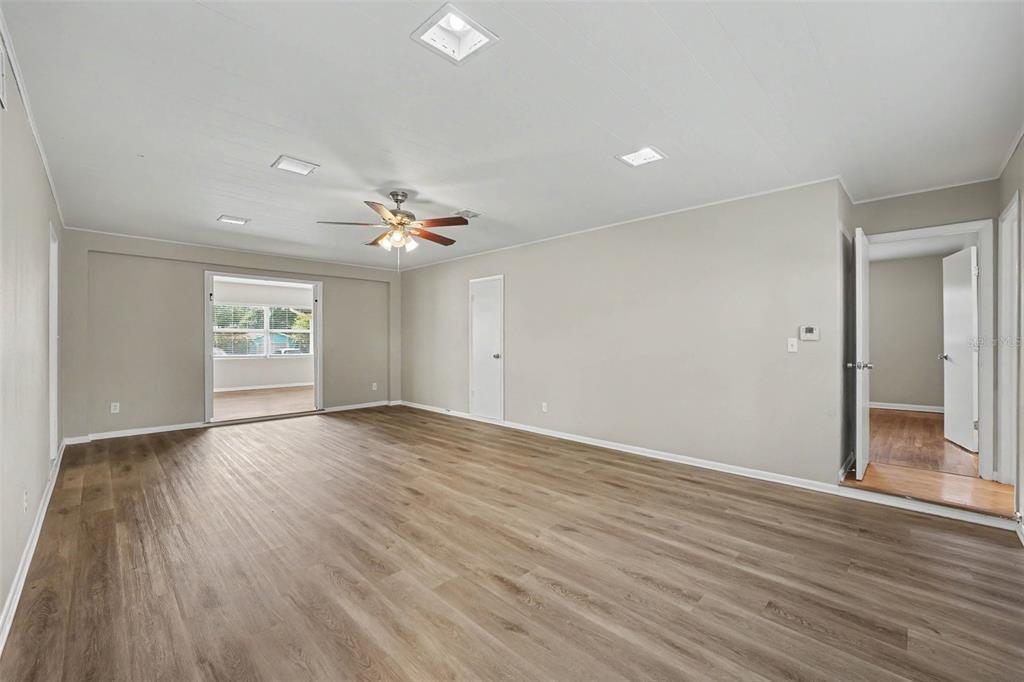 A spacious room with light wood-look flooring, a ceiling fan, and a doorway to a sunroom — 2935 WOODLAND HILLS AVENUE, LAKELAND, FL