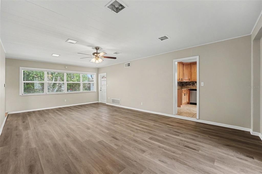 An empty living room features wood-look flooring, a ceiling fan, and a doorway to a kitchen — 2935 WOODLAND HILLS AVENUE, LAKELAND, FL