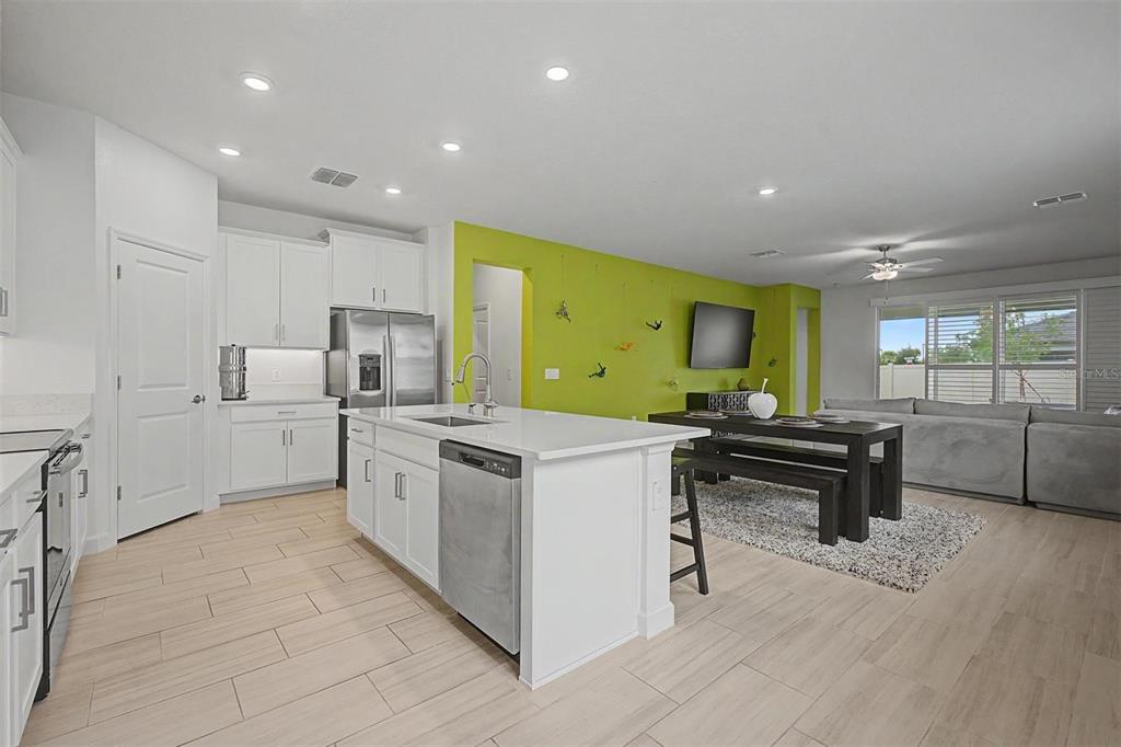 A kitchen with white cabinets and an island opens into a living area with lime-green walls — 10733 TUPPER CAY DRIVE, SAN ANTONIO, FL