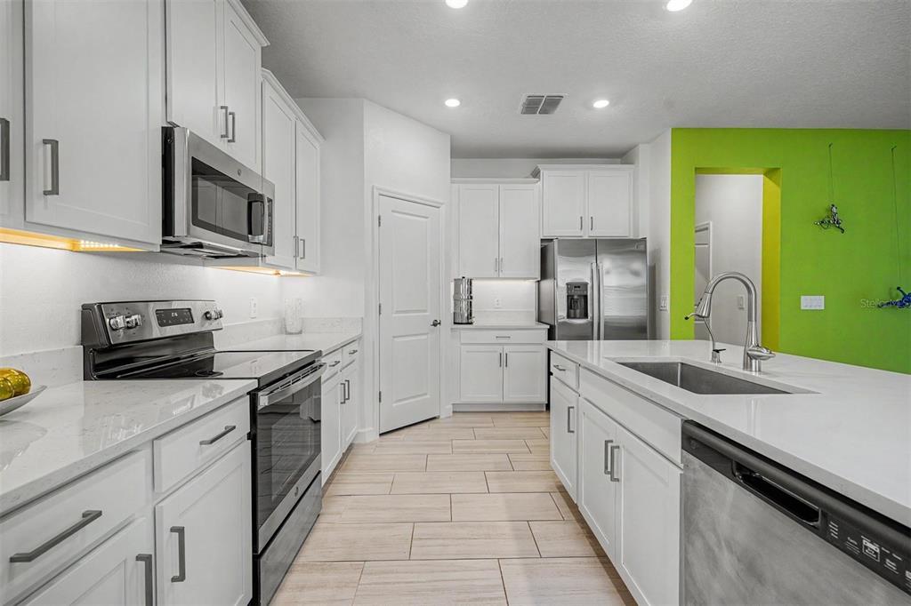 A modern kitchen features white cabinetry, stainless steel appliances, quartz countertops, and a lime-green wall — 10733 TUPPER CAY DRIVE, SAN ANTONIO, FL