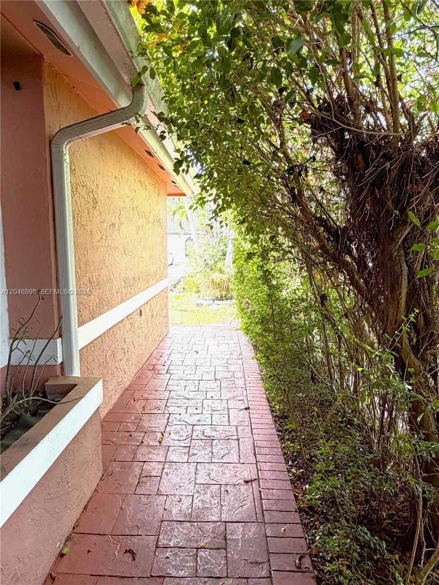 A narrow, red-tiled walkway runs alongside a peach-colored exterior wall and dense green foliage — 14225 SW 55th St, Miami FL 33175, MIAMI, FL