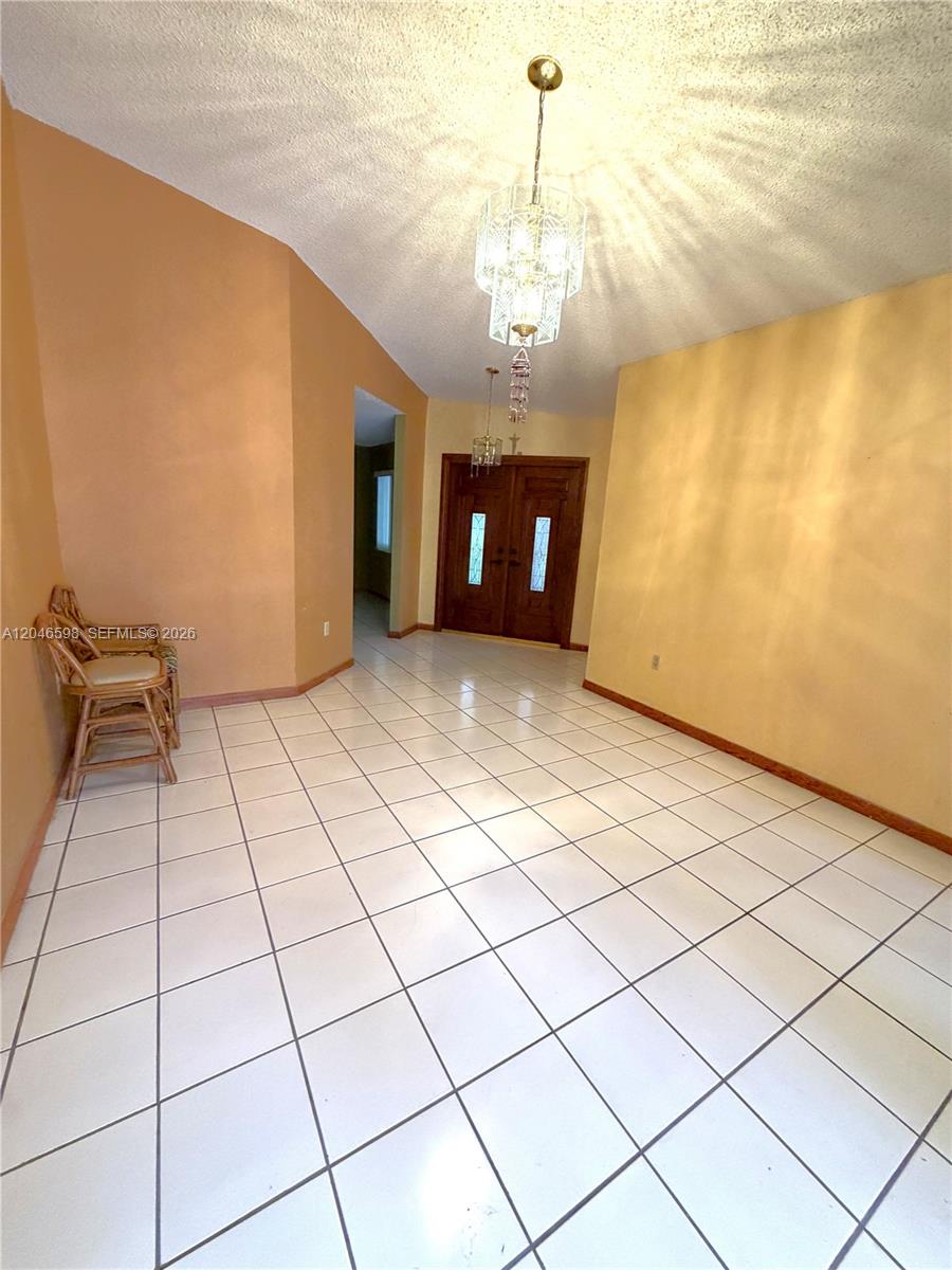 An entryway features white tile floors, a crystal chandelier, and double wooden front doors — 14225 SW 55th St, Miami FL 33175, MIAMI, FL