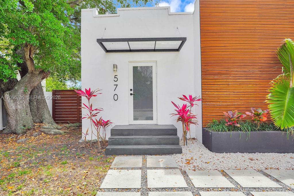 The exterior of a modern home features a white facade, wood siding, and stone steps — 570 NW 48th St, Miami FL 33127, MIAMI, FL