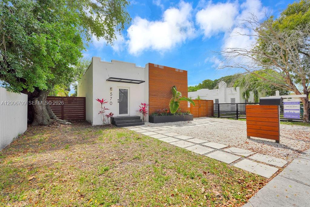 A modern house with a wood-paneled facade and a gravel driveway sits under a blue sky — 570 NW 48th St, Miami FL 33127, MIAMI, FL