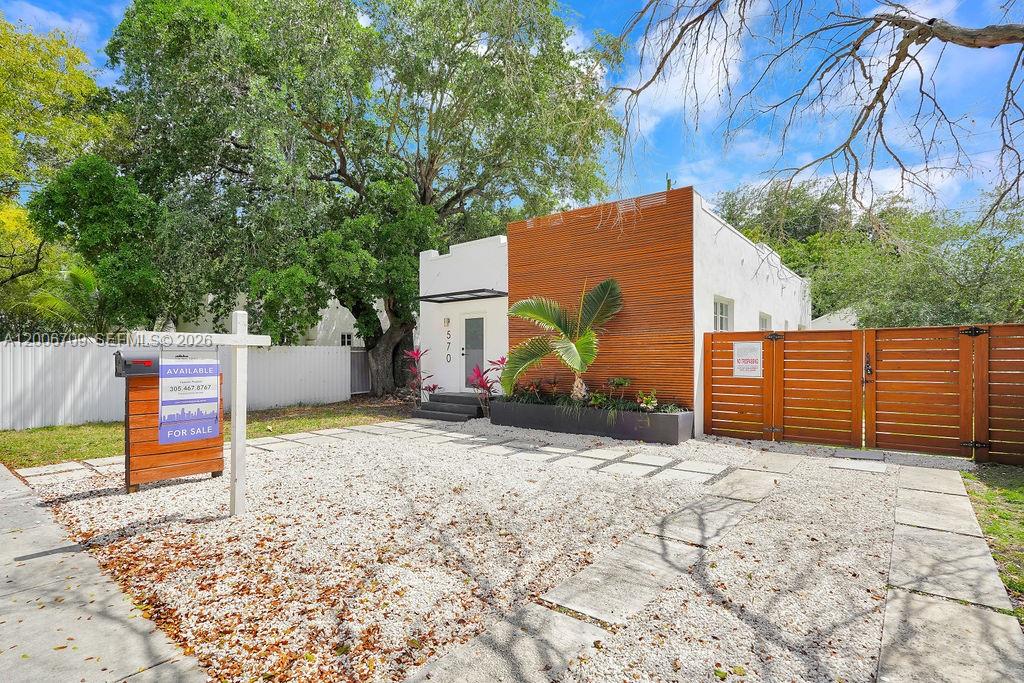 A modern white house with wood-slat siding features a gravel driveway and a wooden gate — 570 NW 48th St, Miami FL 33127, MIAMI, FL