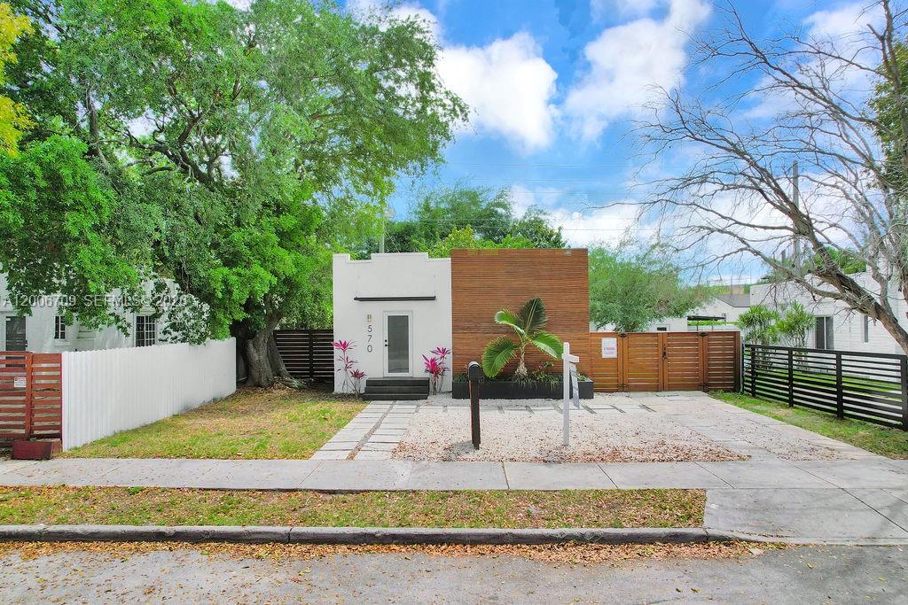 A modern single-story house with a white facade, wood paneling, and a gravel driveway — 570 NW 48th St, Miami FL 33127, MIAMI, FL