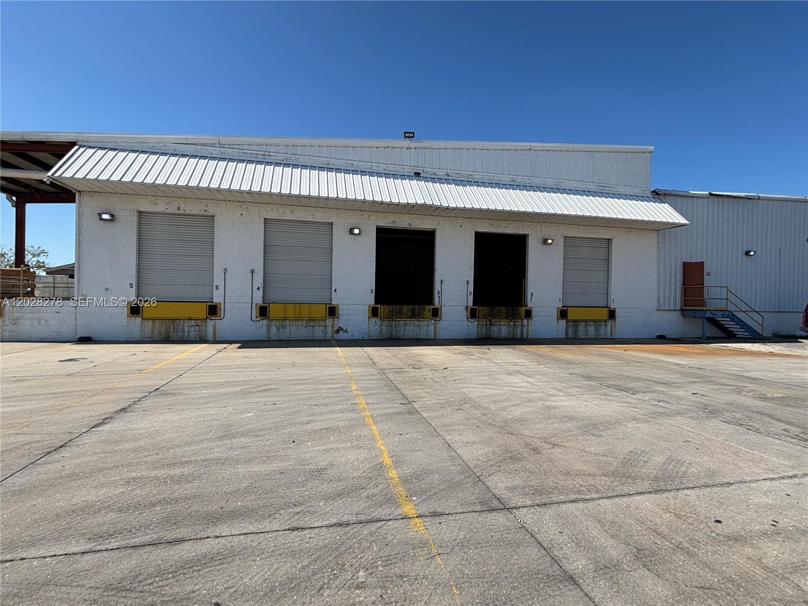 The exterior of a warehouse building features five loading dock bays under a metal awning — 15877 E SR 80, Clewiston FL 33440, CLEWISTON, FL