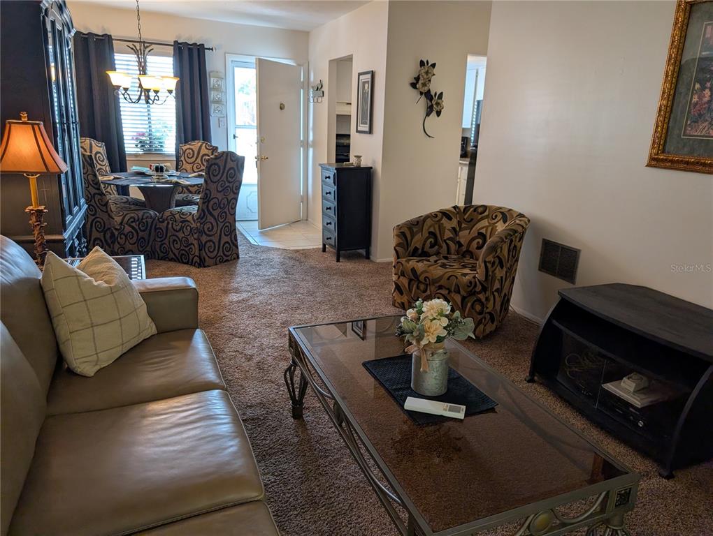 A living room features a leather sofa, glass coffee table, patterned armchair, and dining area — 5864 WELCOME ROAD UNIT J-26, BRADENTON, FL