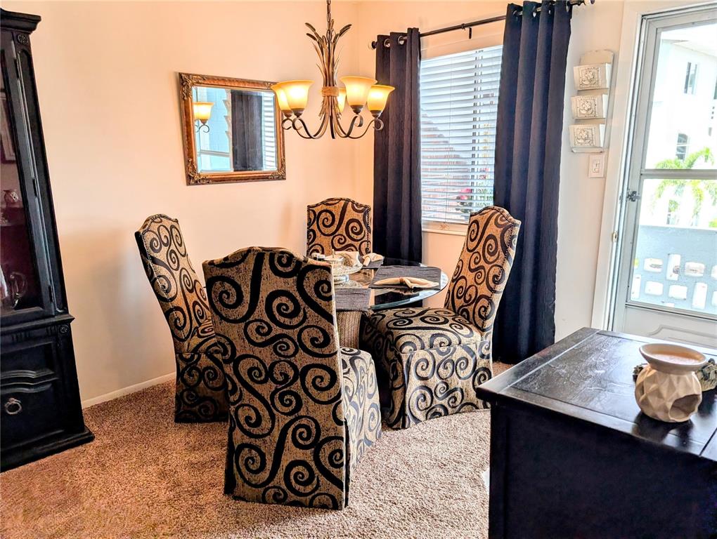 A dining area features a glass-topped table with four patterned chairs under a chandelier — 5864 WELCOME ROAD UNIT J-26, BRADENTON, FL
