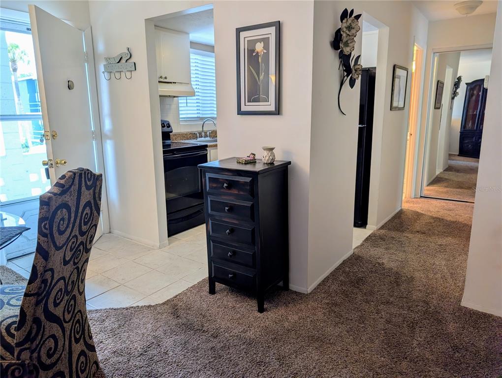 A dark wooden chest of drawers sits between a tiled kitchen and a carpeted hallway — 5864 WELCOME ROAD UNIT J-26, BRADENTON, FL