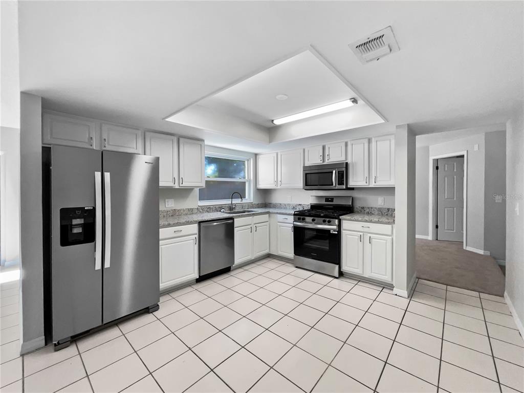 A kitchen with white cabinets, stainless steel appliances, granite countertops, and white tiled flooring — 831 HAULOVER DRIVE, ALTAMONTE SPRINGS, FL