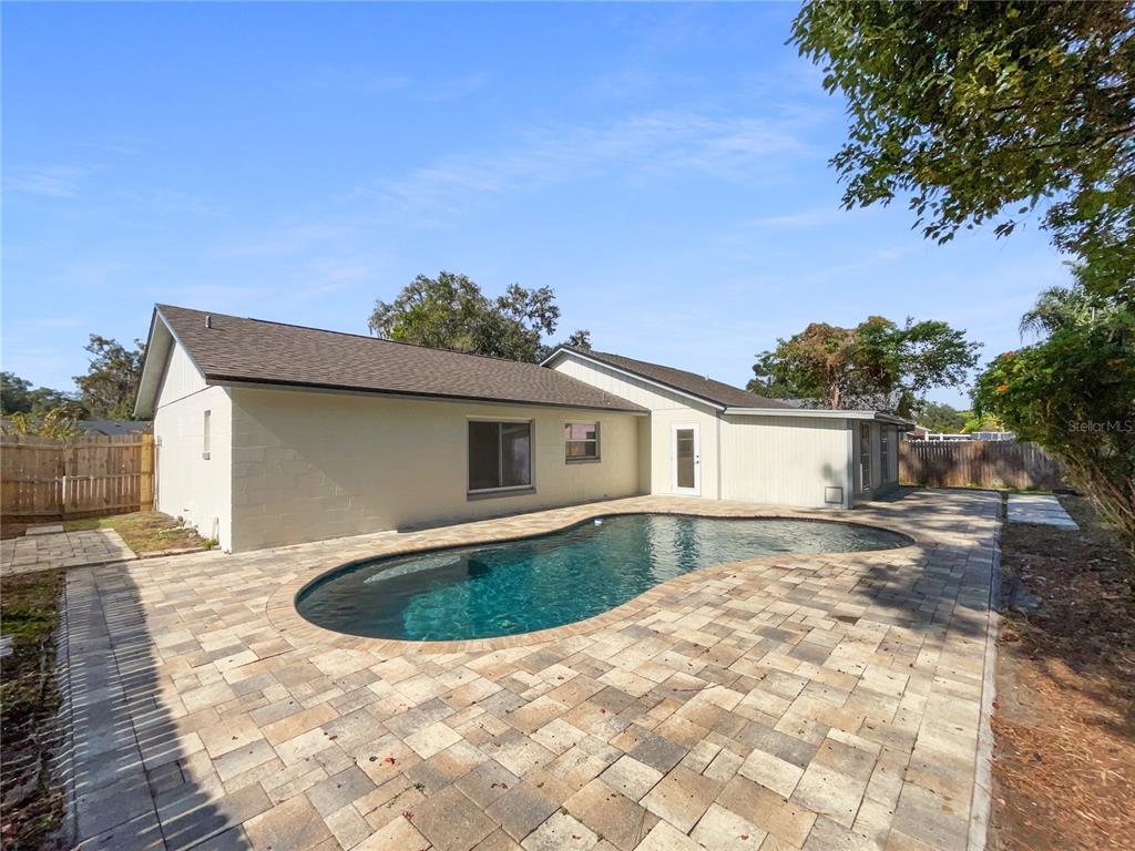 A backyard features a kidney-shaped swimming pool surrounded by a light-colored paver patio — 831 HAULOVER DRIVE, ALTAMONTE SPRINGS, FL