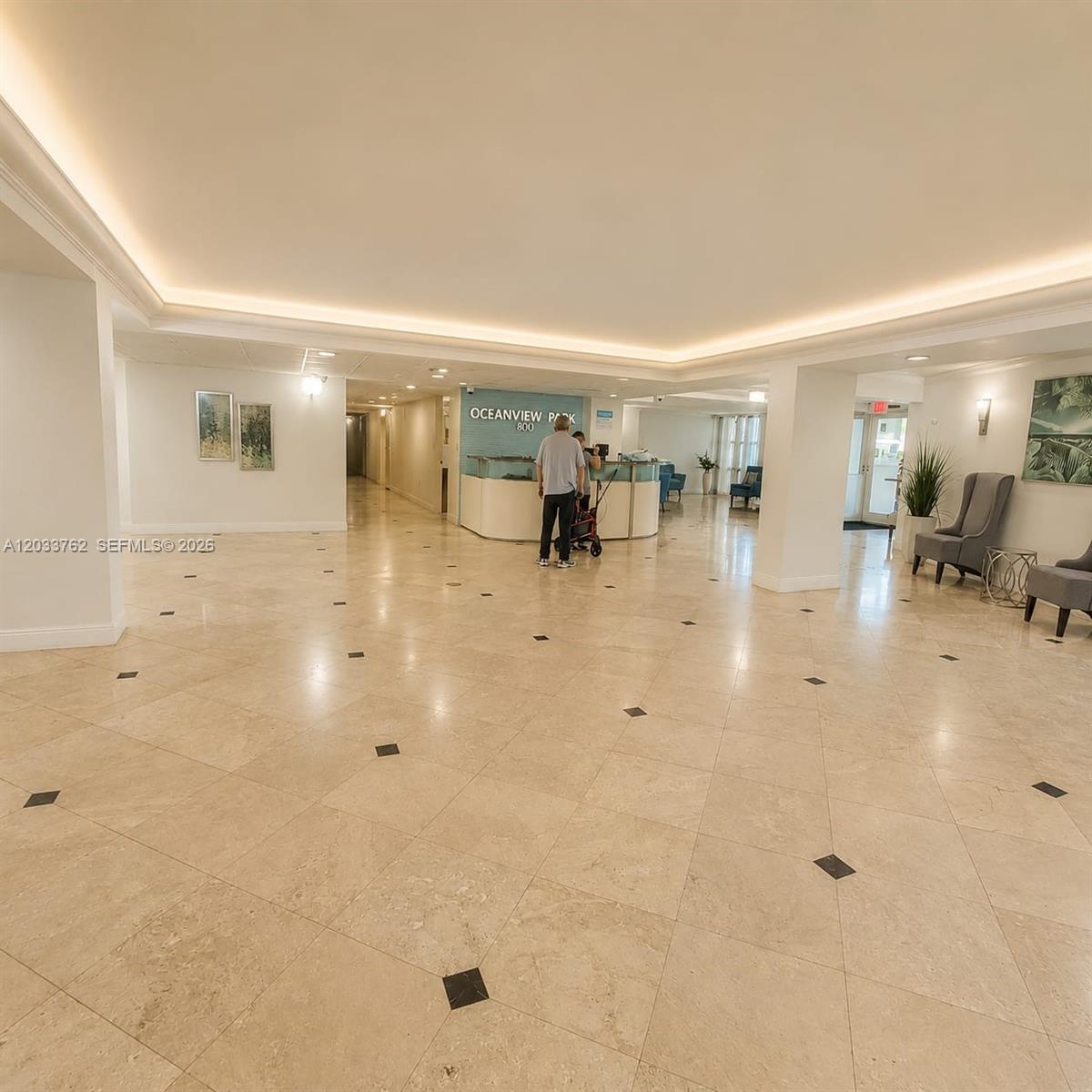 A spacious building lobby features light-colored tile floors, recessed ceiling lighting, and a reception desk — 800 Parkview Dr # 512, Hallandale Beach FL 33009, HALLANDALE BEACH, FL