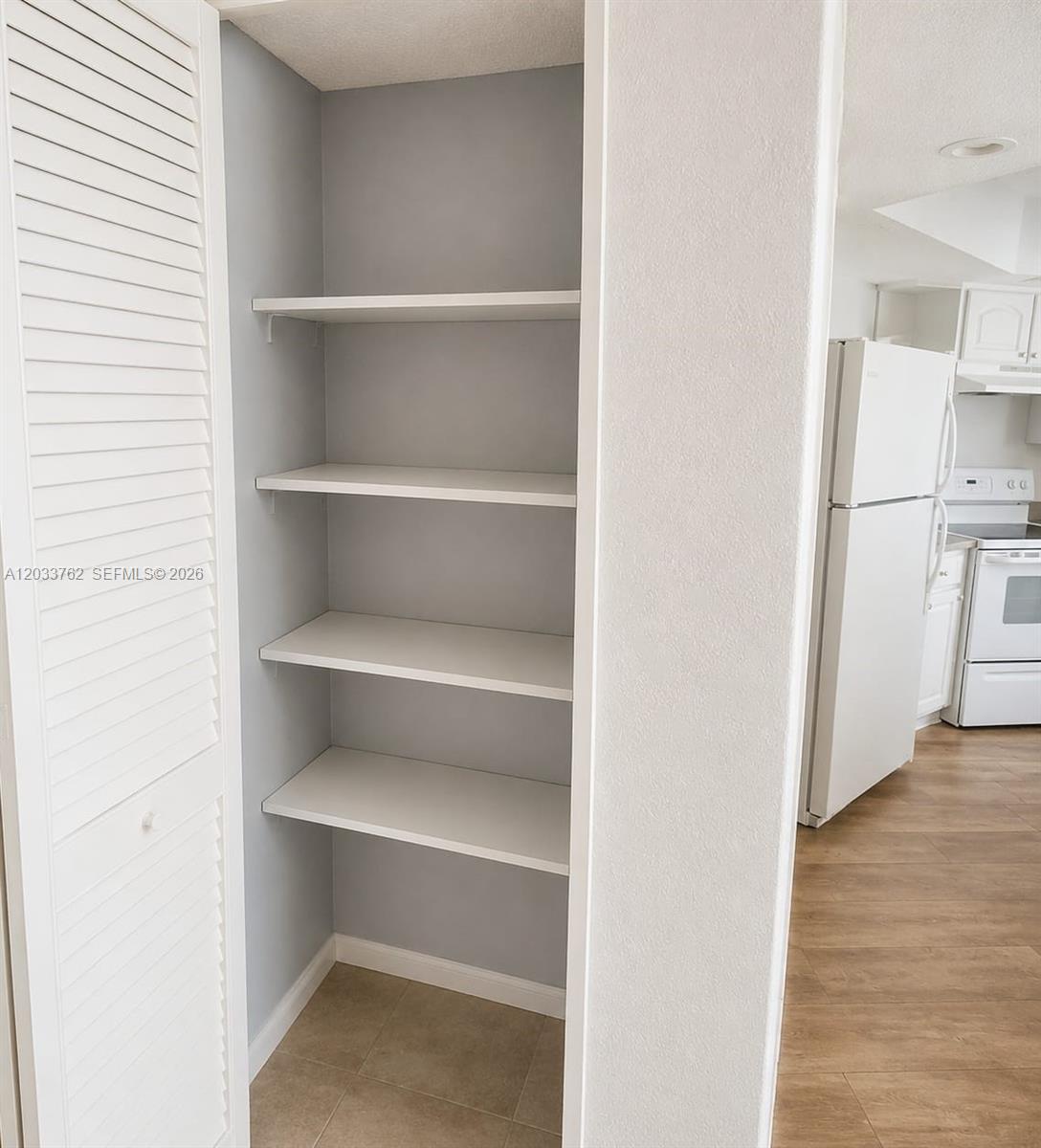 A pantry with four white shelves is situated next to a kitchen with white appliances — 800 Parkview Dr # 512, Hallandale Beach FL 33009, HALLANDALE BEACH, FL