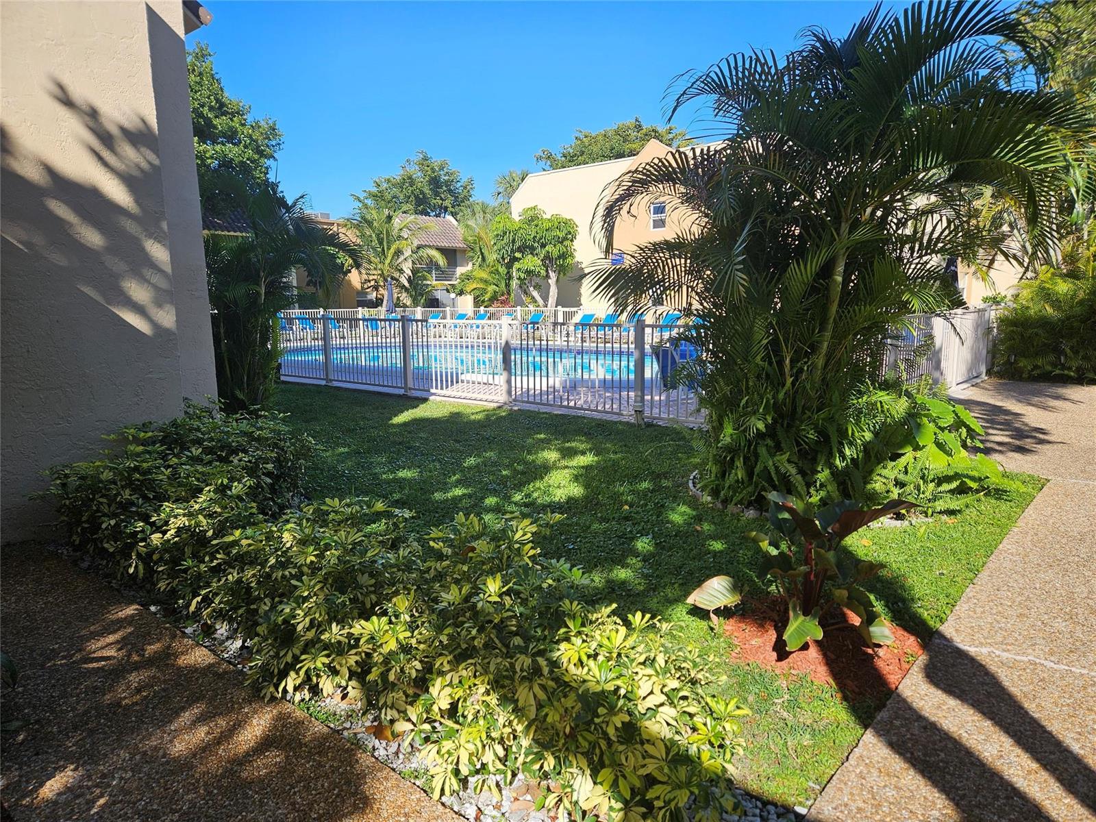 A fenced swimming pool sits in a courtyard surrounded by palm trees and apartment buildings — 959 SE 2nd Avenue # 117, Deerfield Beach FL 33441, DEERFIELD BEACH, FL