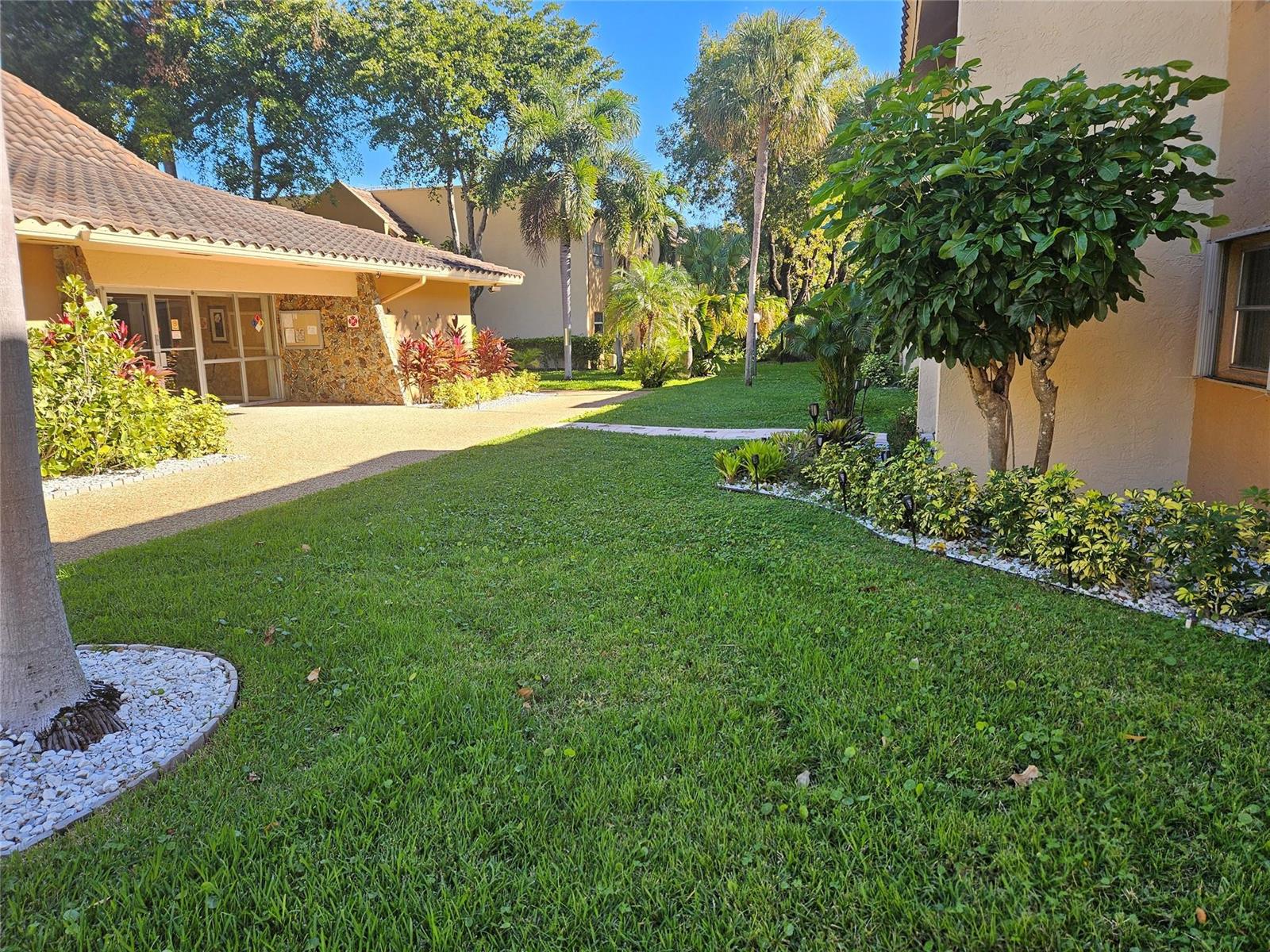 A grassy courtyard with palm trees and landscaping sits between two tan stucco apartment buildings — 959 SE 2nd Avenue # 117, Deerfield Beach FL 33441, DEERFIELD BEACH, FL
